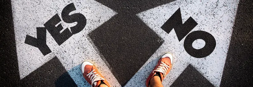 A person's feet wearing orange sneakers standing on pavement with large "YES" and "NO" text painted on the ground